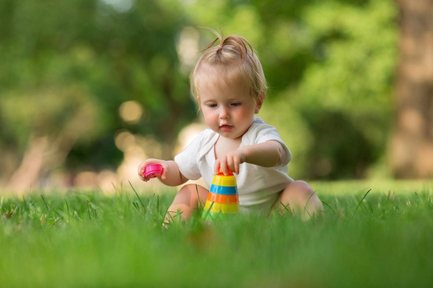 Toddler on grass stacking a colourful plastic pyramid of rings